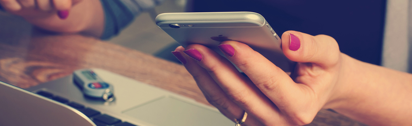 Close shot of a nail painted female hand with iphone and a laptop nearby