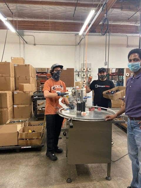 Three workers wearing masks packaging hand sanitizers