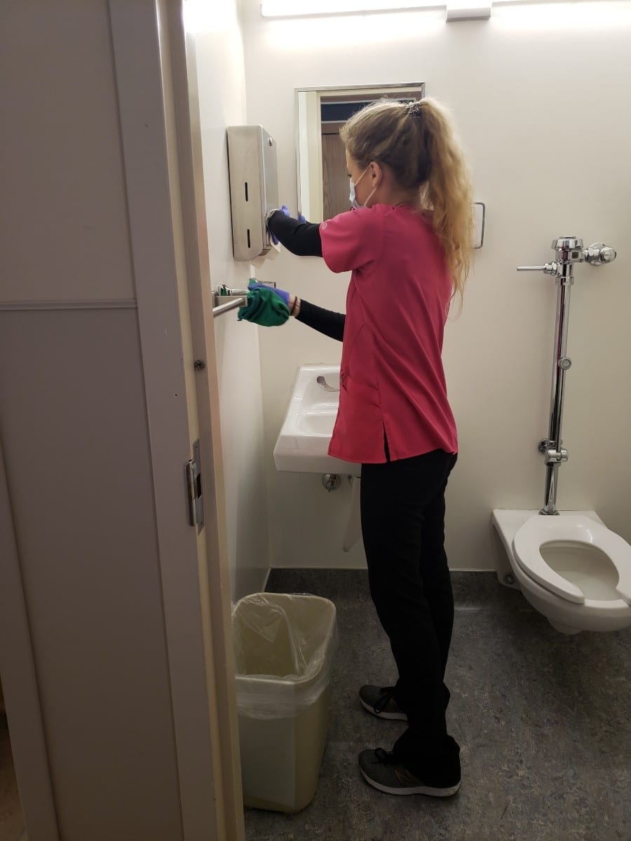 Team member Lauren wearing a mask and cleaning the restroom