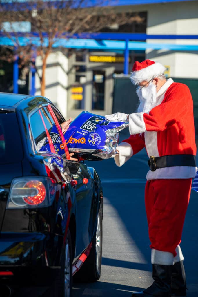 A man dressed up as Santa Claus handing over holiday basket to a person inside a car