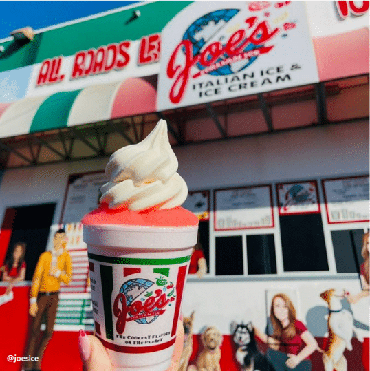 A hand holding Joe’s Italian Ice cream infront of the Joe's shop