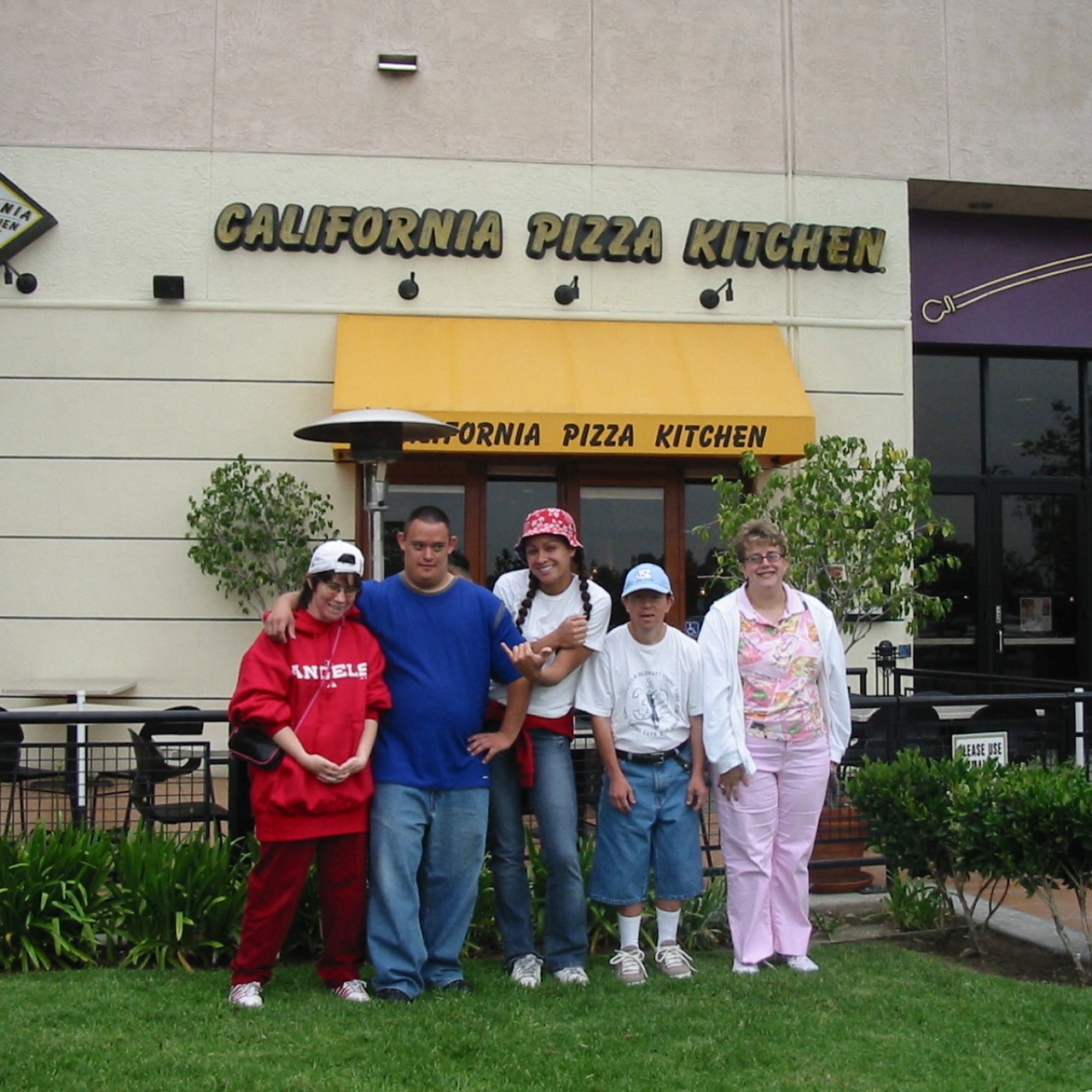 A group of employees from Goodwill are standing in front of the California Pizza Kitchen restaurant.