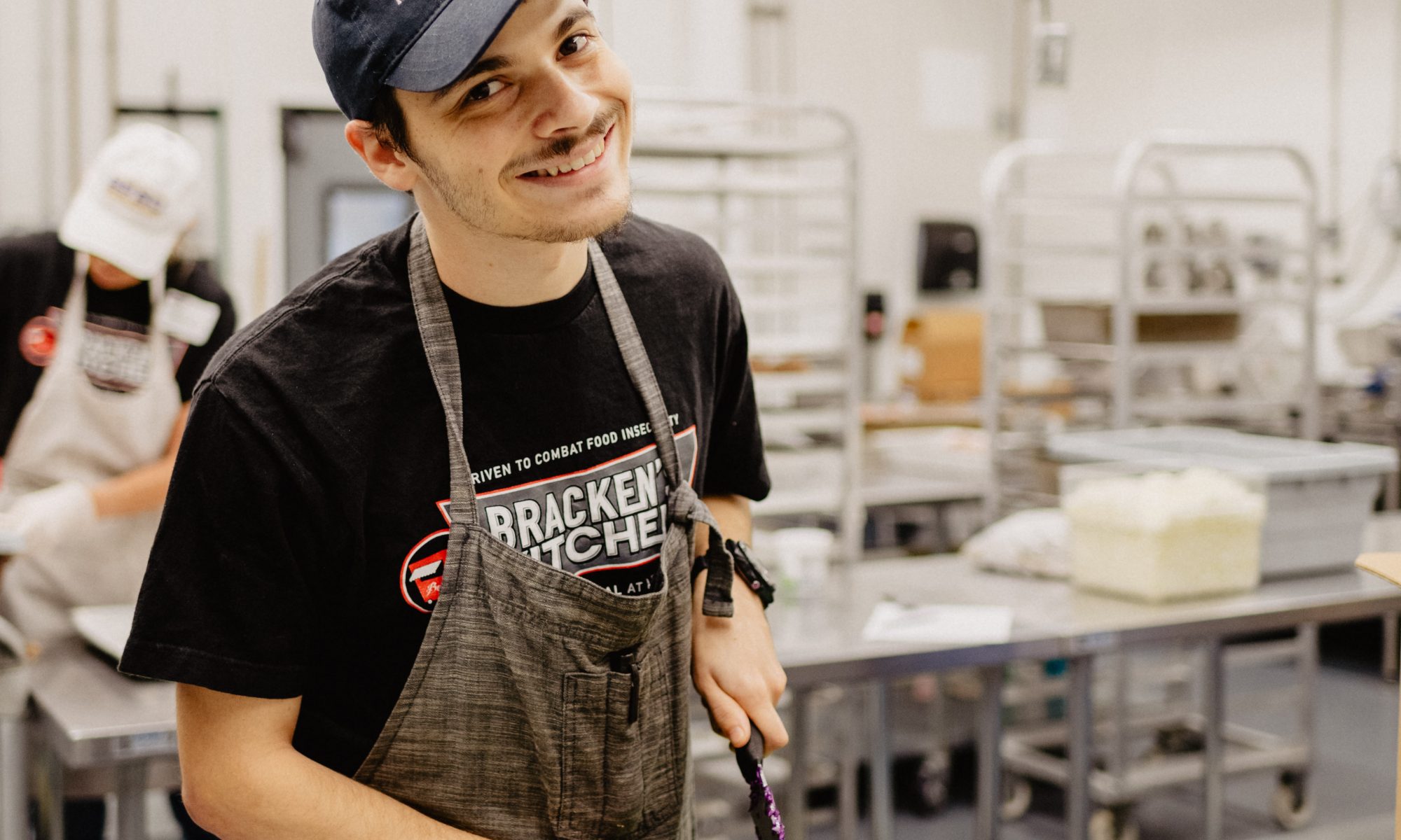 A man poses in a commercial kitchen as he chops vegetables