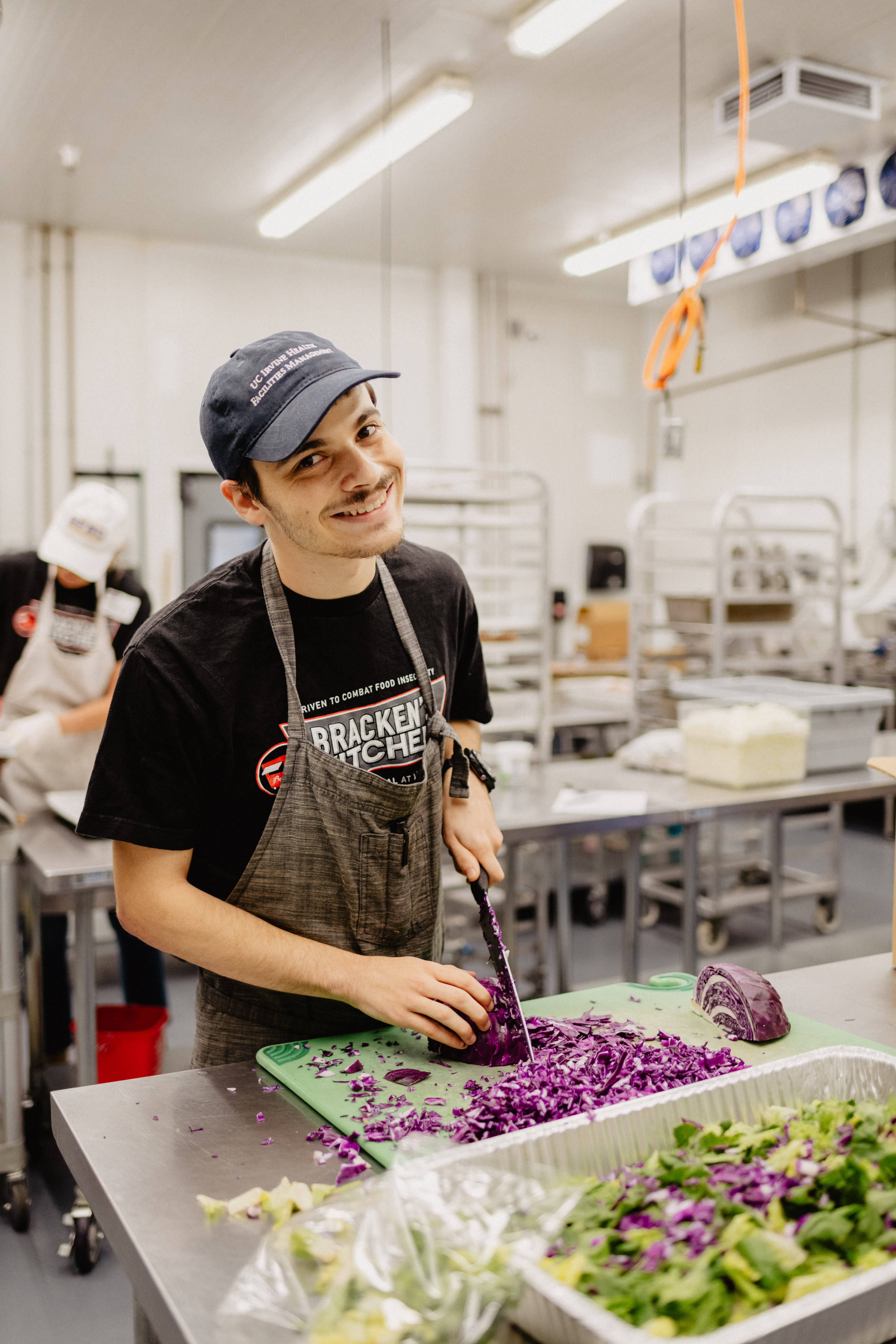 A man poses in a commercial kitchen as he chops vegetables